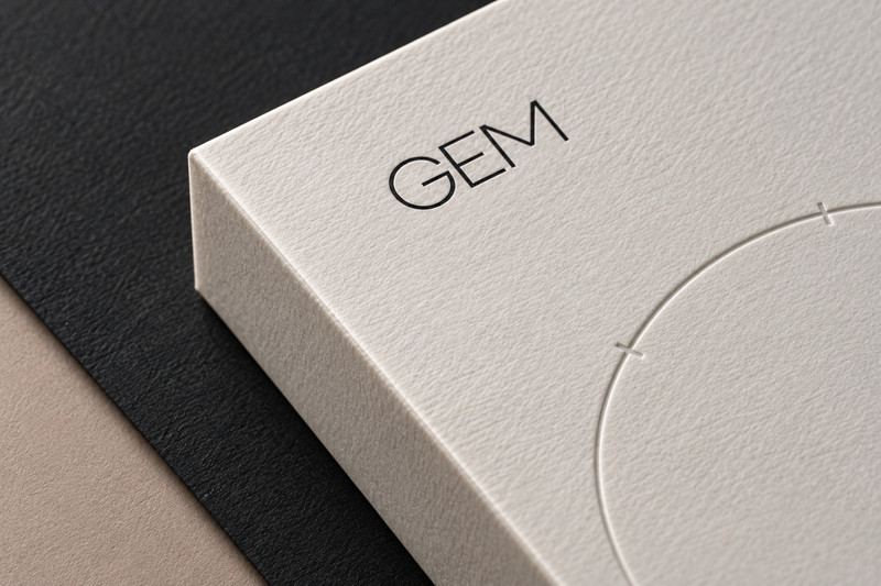 Close view of textured ivory GEM packaging, a debossed arc and contrasting dark material.
